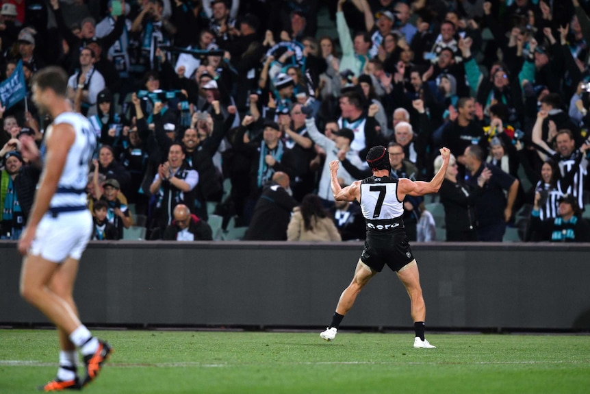 An AFL footballer stands in front of a cheering crowd and pumps his fists in celebration.