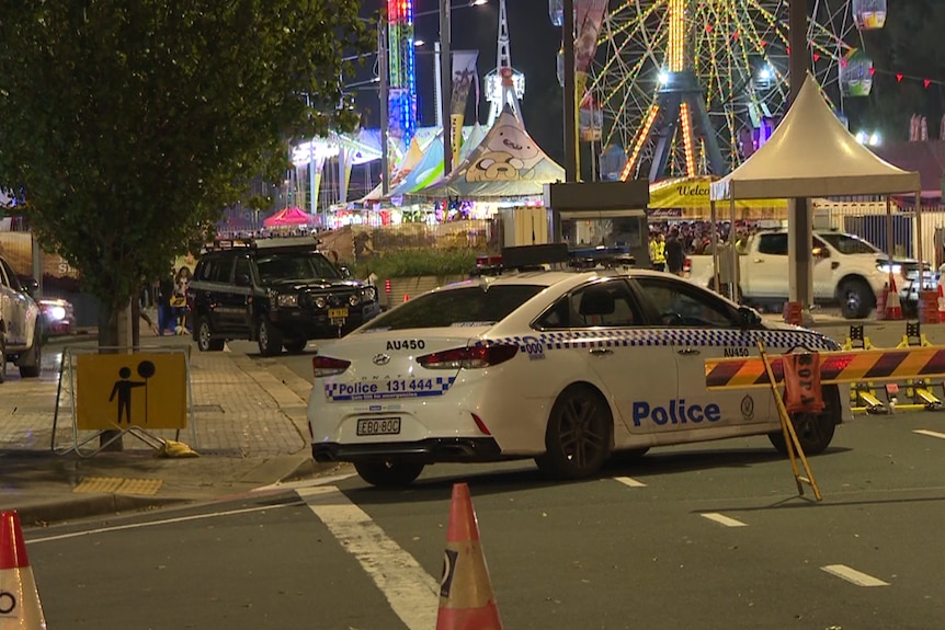 A car in the forefront with a festival and the rides in the background