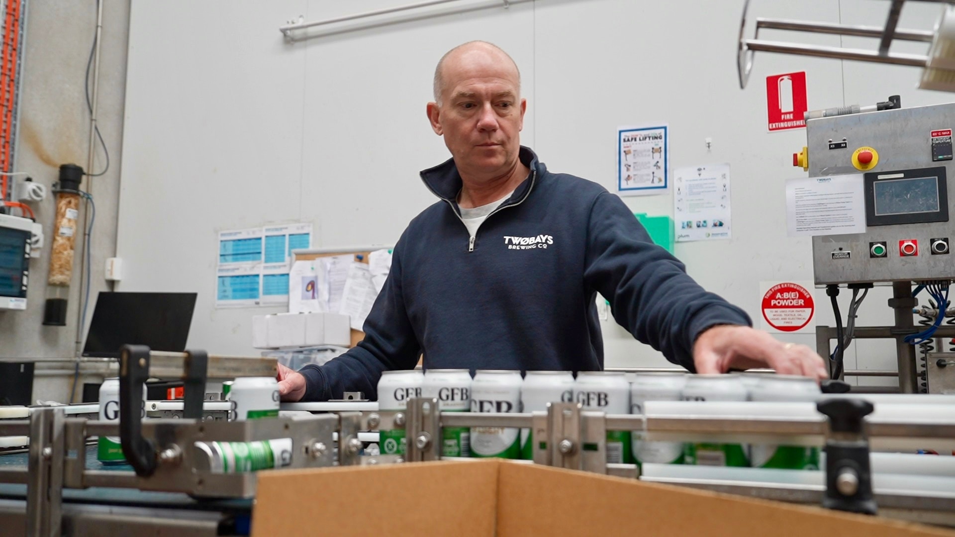 Richard Jeffares veste um suéter azul e verifica latas de cerveja em uma linha de produção.