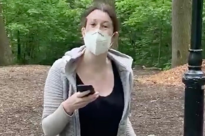 Brunette woman wearing grey jacket, black shirt and jeans, wearing mask, holding phone and yellow dog