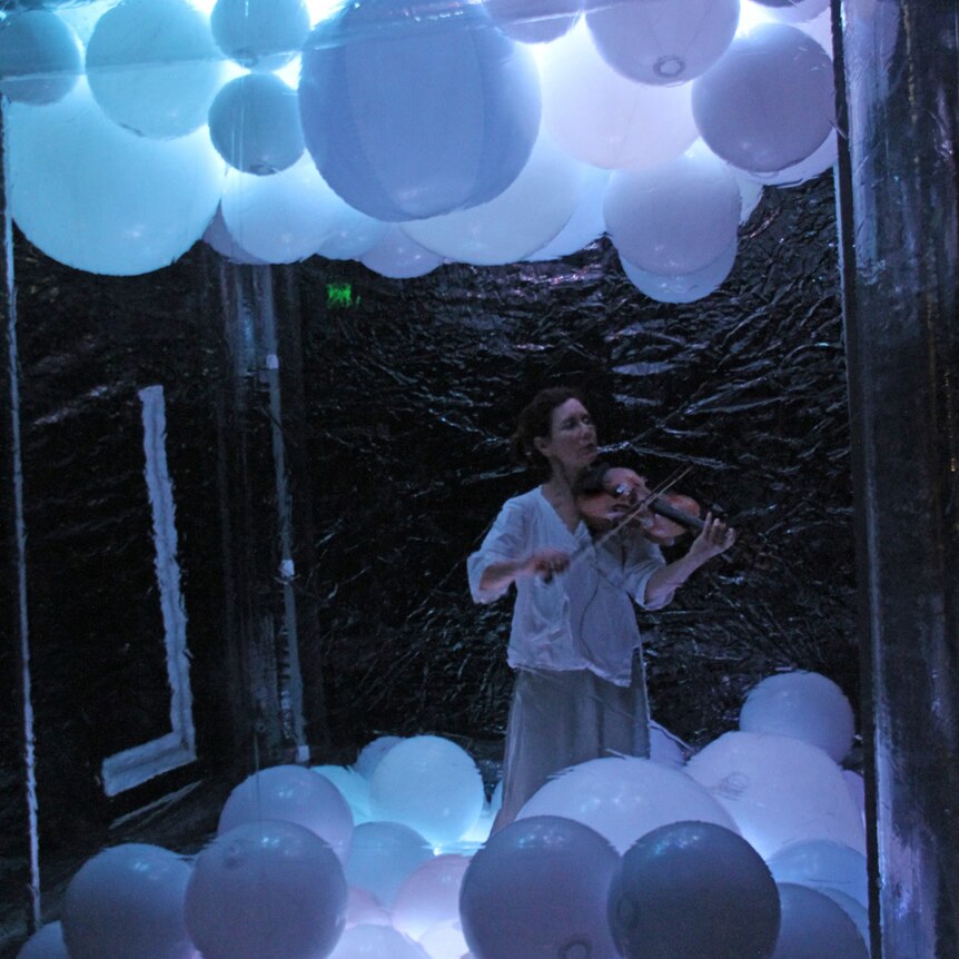 Violinist Anna McMichael stands in a cube surrounded by bubbles