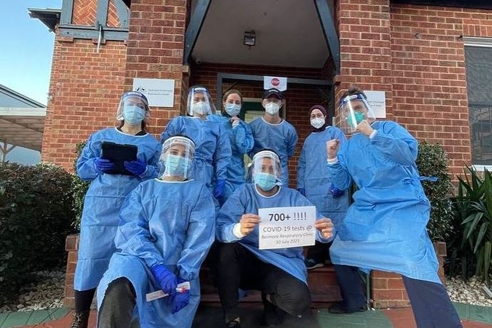Eight medical staff wearing PPE including masks and face shields stand with a sign that reads 700+ COVID-19 tests