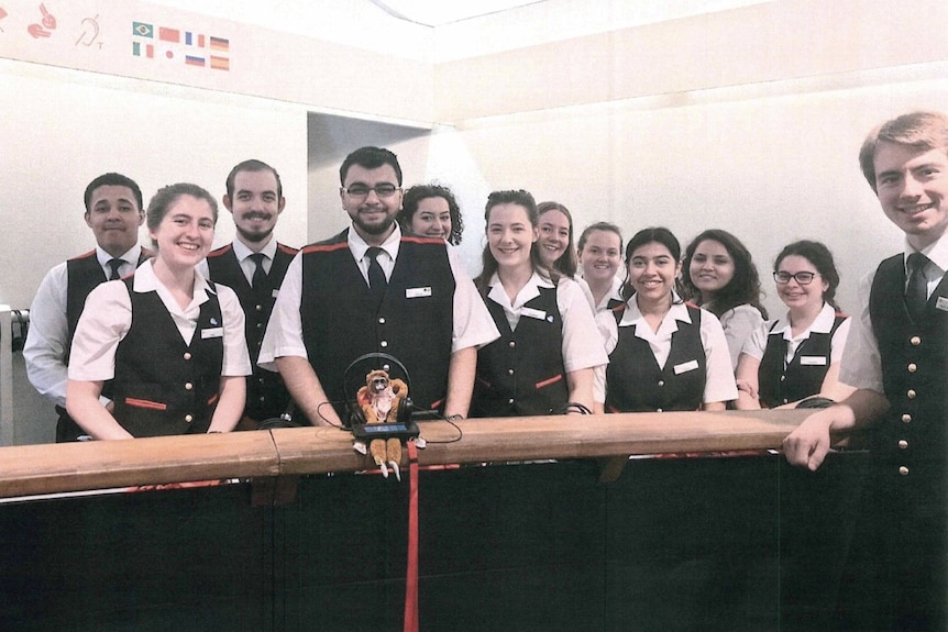 A toy monkey with 12 people wearing white shirts and black vests