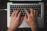 Close-up shot of two hands with dark-ish hair on them on the keyboard of a silver laptop.
