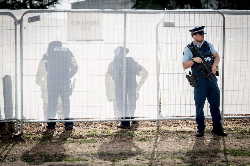 Police officers stand at a tarp-covered fence with guns.