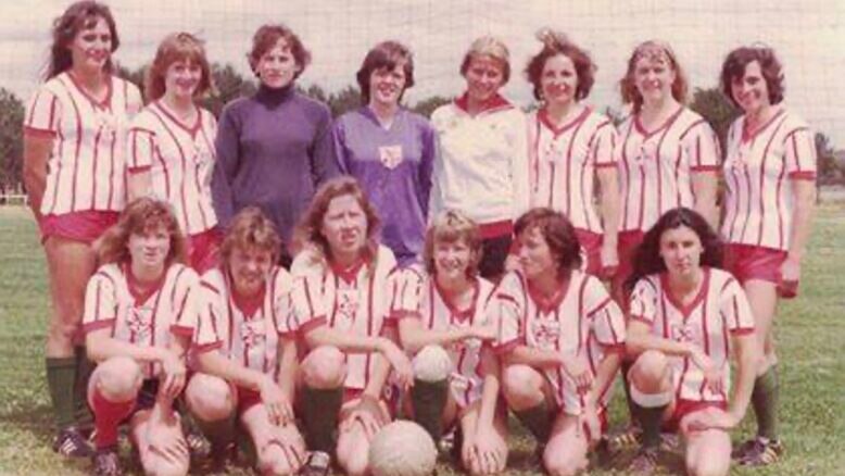 A women's soccer team wearing white and red striped uniforms pose for a team photo before a game
