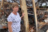 A woman stands in front of debris from a fire