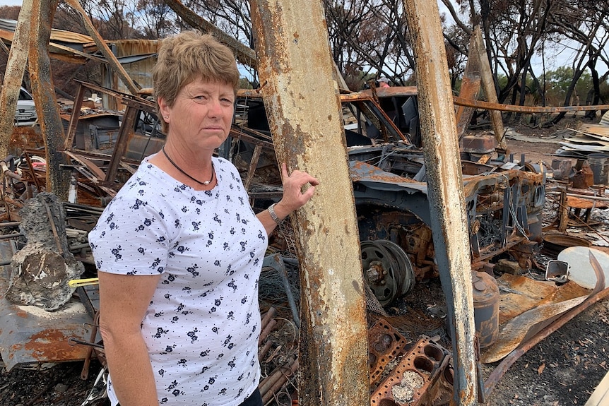 A woman stands in front of debris from a fire