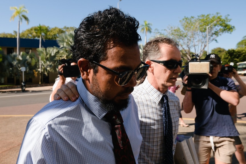 A man walks next to his laywer towards a court in Darwin. Camerapeople film him.