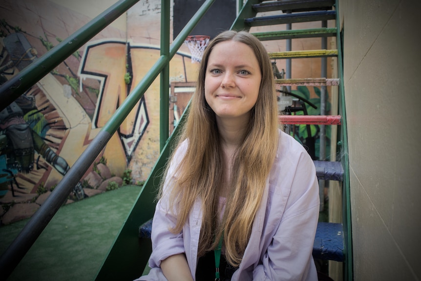 Hannah Giles sits on some colourful steps, smilling in a portrait.