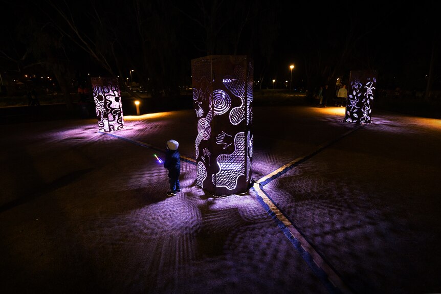young child stands in the dark at the base of an installation of lights