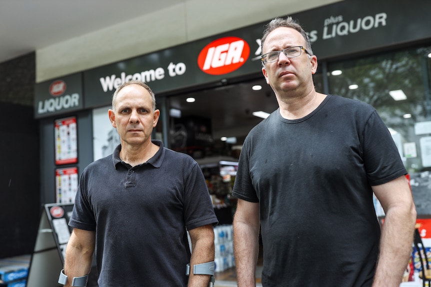 Two men standing outside a supermarket, frowning