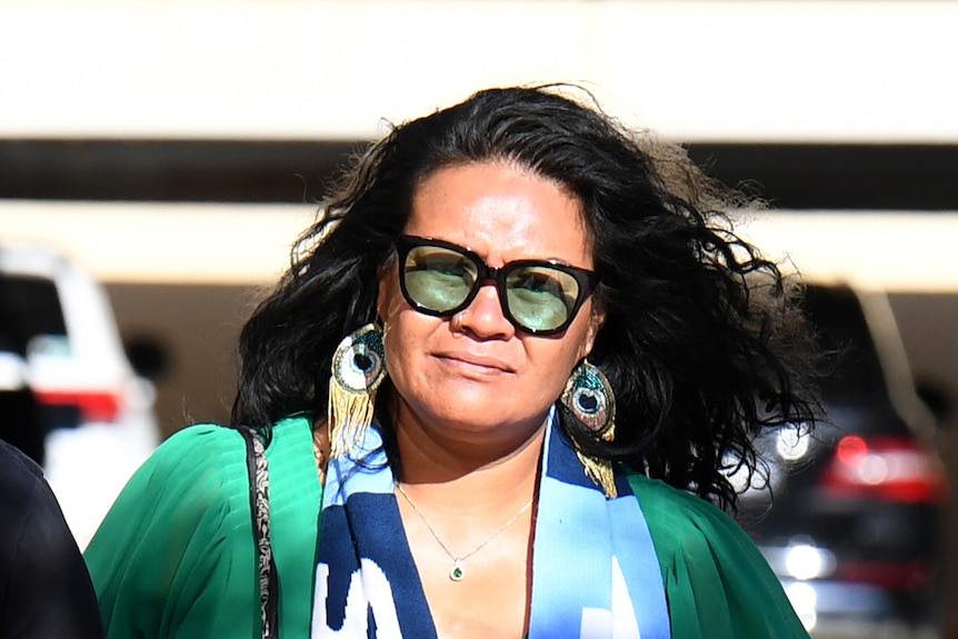 A woman with dark hair, wearing sunglasses and a football scarf.