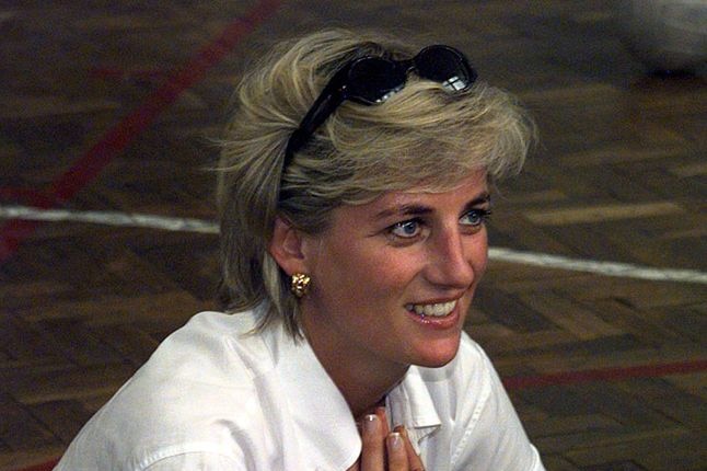 Princess Diana is couching down on the floor and is smiling