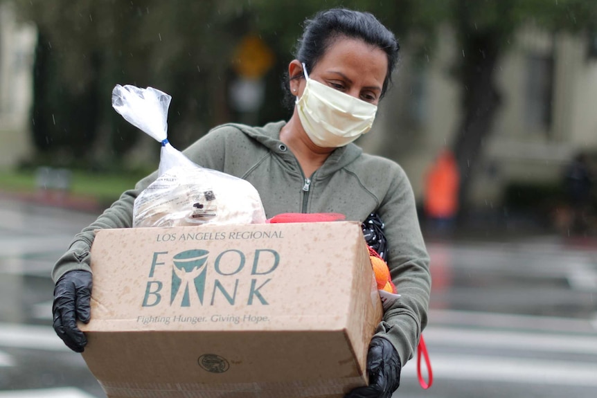A woman in a face mask carrying a box of food
