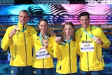 Swimmers wearing yellow jackets hold up medals and pose for a photo after winning a race
