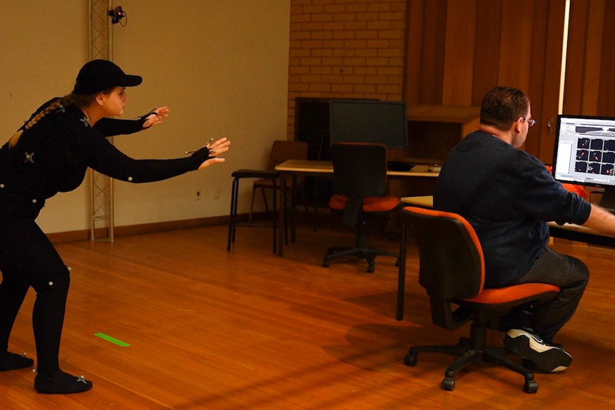 man works at computer while actor in motion capture suit performs move