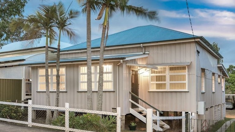 A one-storey beige house with a tin roof on cement stilts.