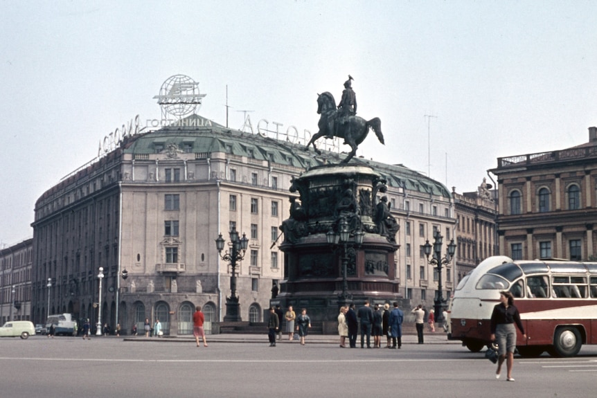 People cross the street near a large statue of a man riding a horse