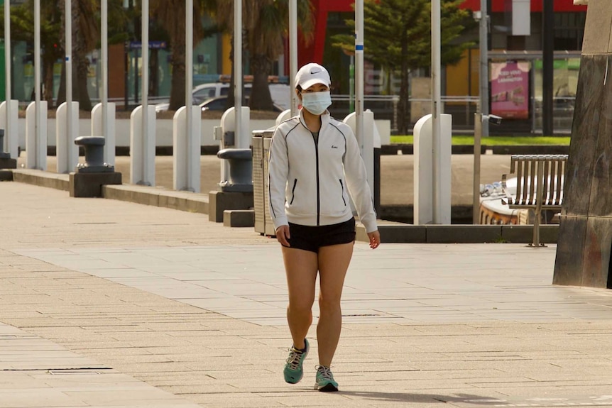 A woman wearing a mask and white cape walks in Melbourne's Docklands.