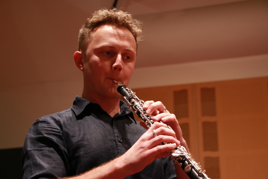 A man with blonde curly hair plays the oboe