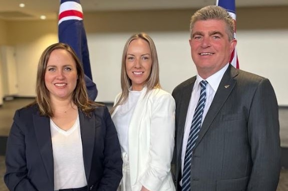 three people standing in front of two Australian flags