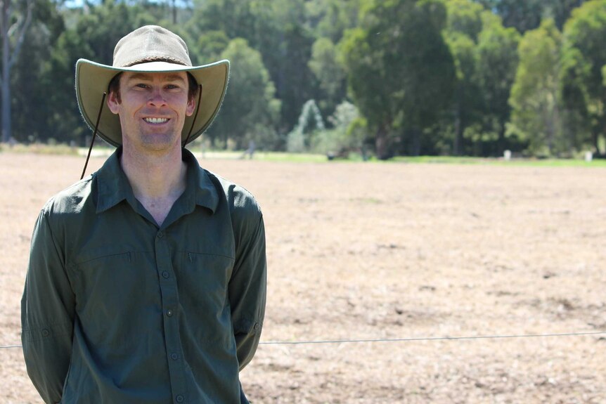 A man in a hat standing in front of a paddock.