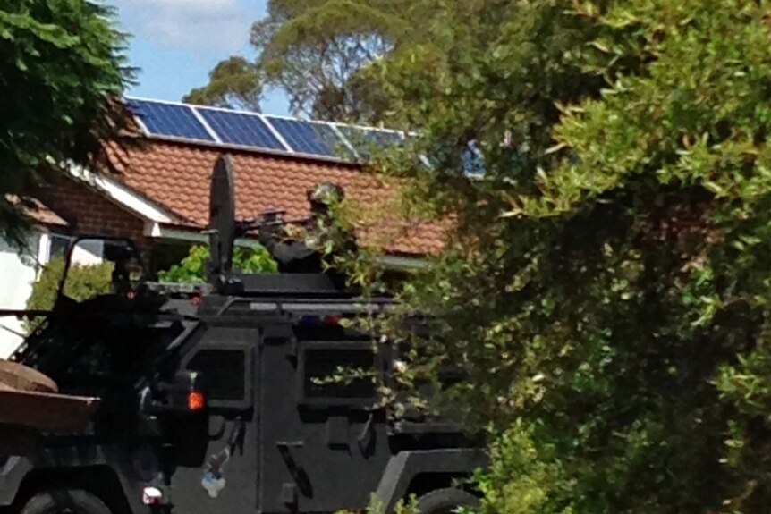 A tactical response officer aims a weapon during a siege on a suburban street