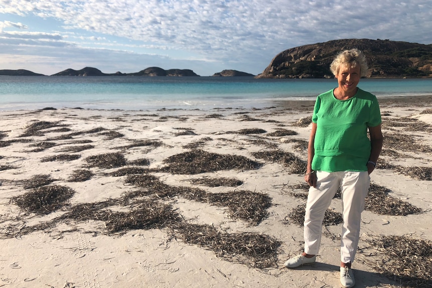 Heather Ewart sands on a sandy beach.