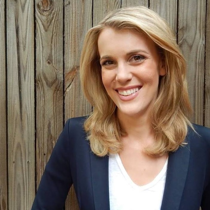 A blonde woman wearing a white shirt and navy jacket, smiling broadly