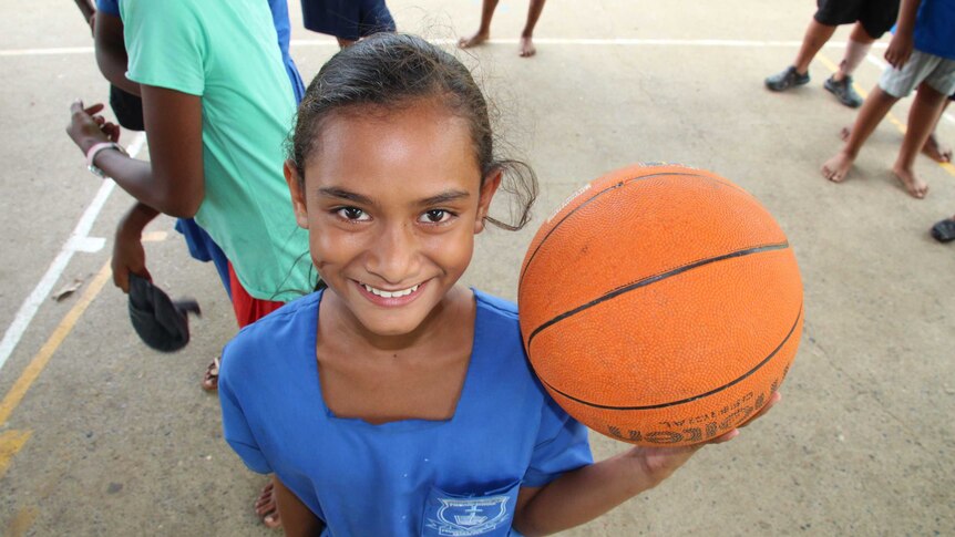 A girl in a school uniform holds a basketball and smiles.