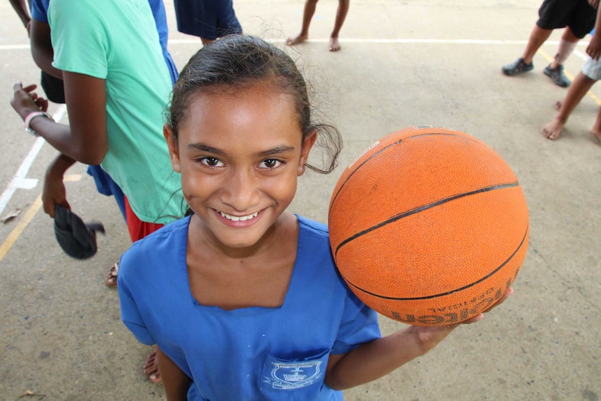 A girl in a school uniform holds a basketball and smiles.