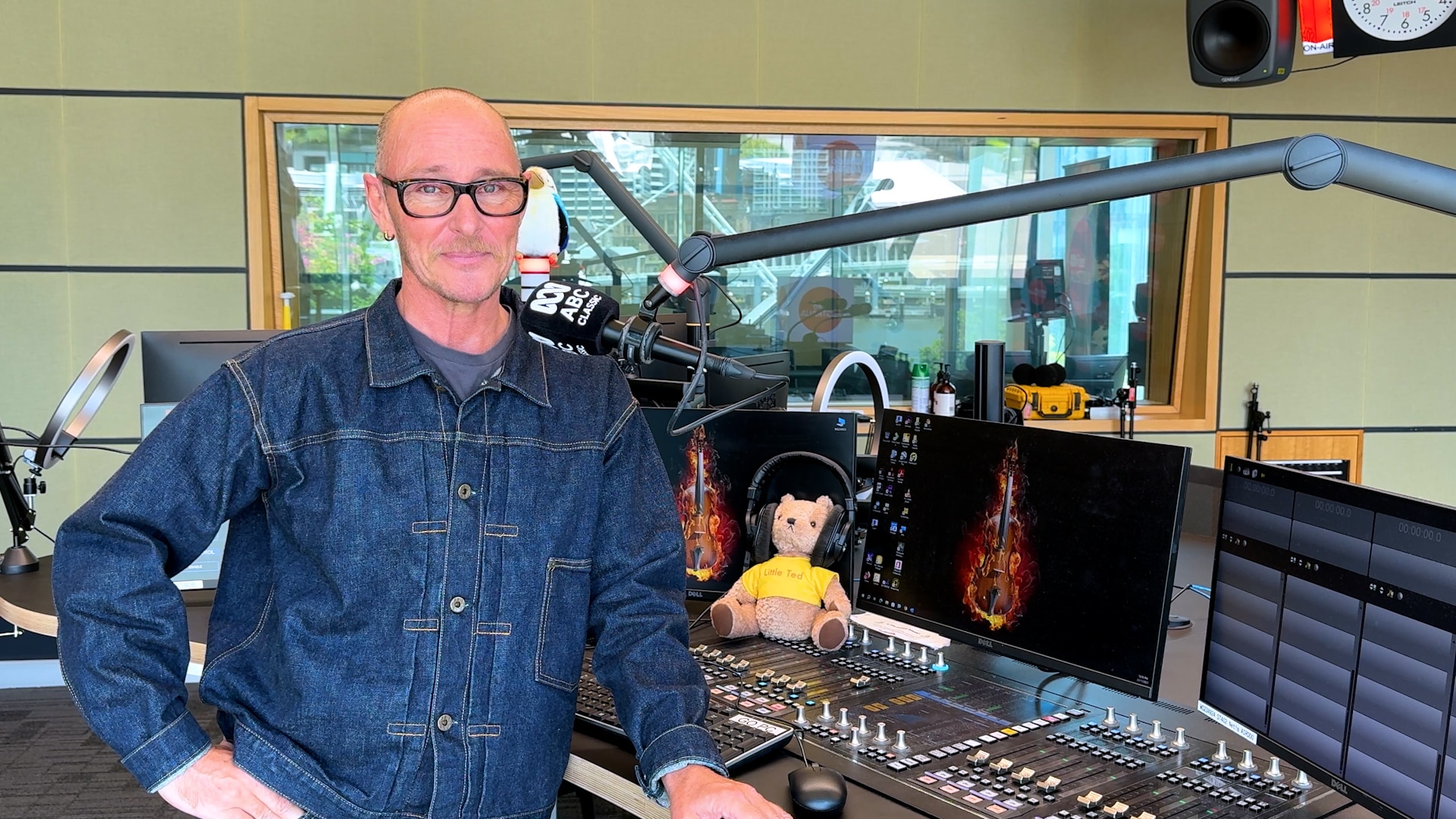 Ed está de pie con un brazo sobre el escritorio del estudio ABC Classic y sonríe a la cámara. 