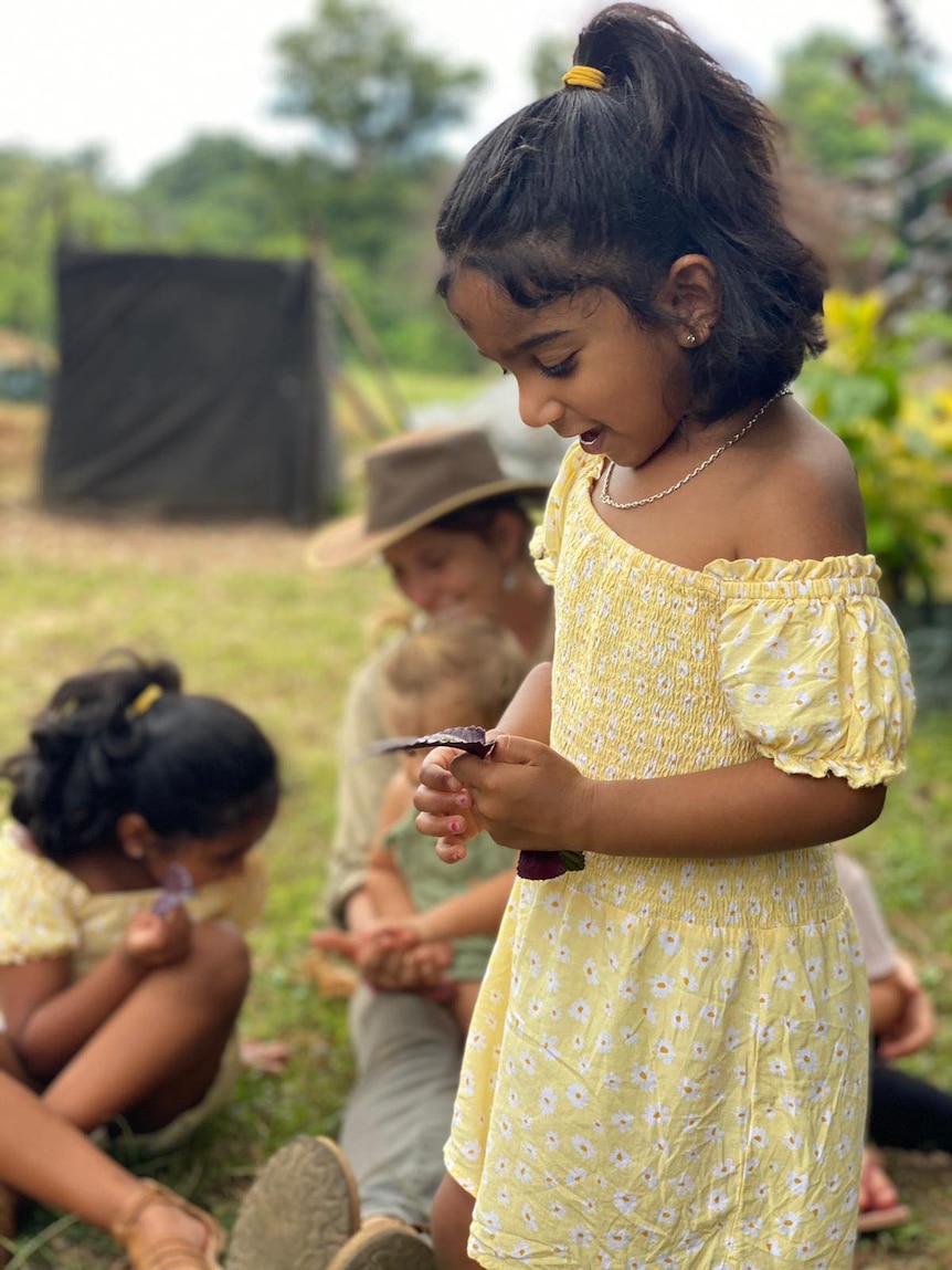 A little girl in a yellow dress holding a leaf.