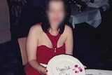 A woman, whose identity has been hidden, sits at a table holding a plate that says "Happy 21st Birthday".