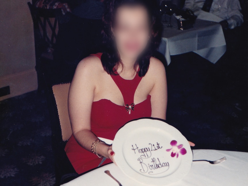 A woman, whose identity has been hidden, sits at a table holding a plate that says "Happy 21st Birthday".