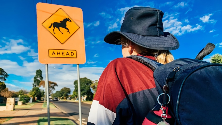 A school student stands in front of a "horse crossing" sign.