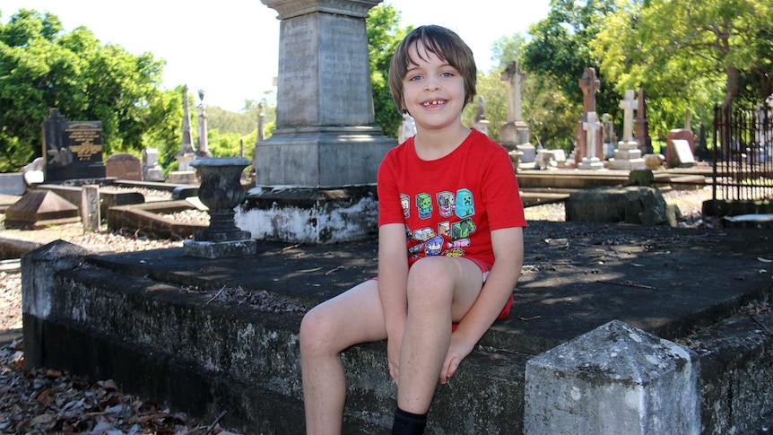 Jack Chenoweth, 7, sits in the South Brisbane Cemetery.