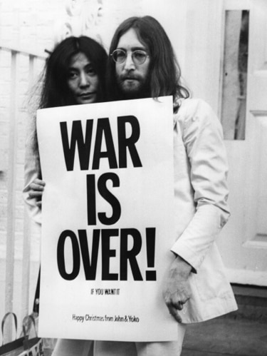 A woman with long dark hair and a man with long hair hold a sign saying 'war is over!'.