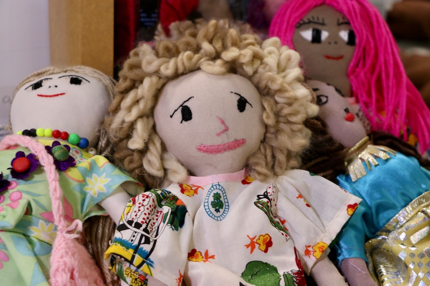 A close-up shot of a group of dolls, with the one in the middle smiling and looking emotional.
