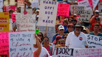 Protesters marching with signs that read "Hands off Roe v Wade" and "Don't trust me with a choice, but with a child?"