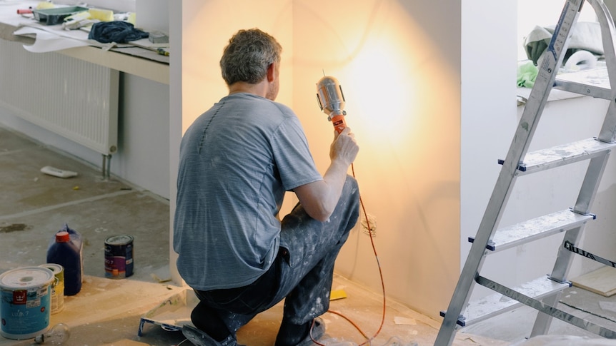 Surrounded by a ladder and paint tins, a tradesman works on a home renovation