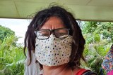 Torres Strait Islander woman with short dreadlocks and glasses wears colourful sewn face mask.