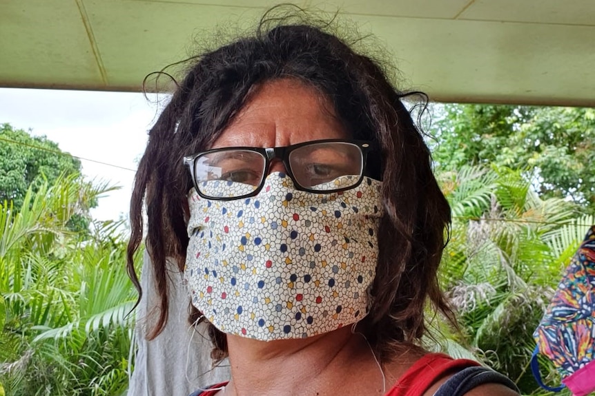 Torres Strait Islander woman with short dreadlocks and glasses wears colourful sewn face mask.
