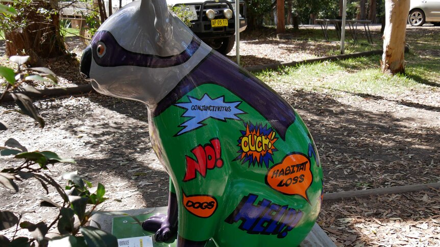 A bright sculpture of a koala, painted with colourful slogans saying habitat loss, ouch, help