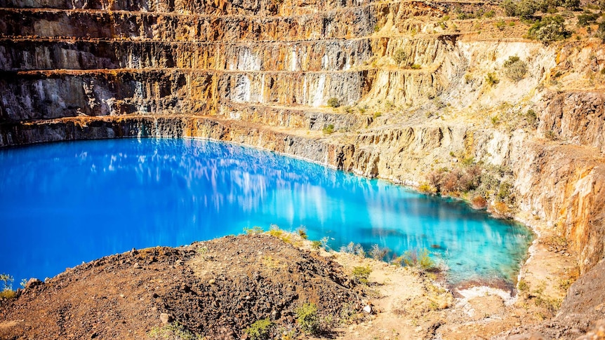 A picture of an old mine pit, showing each level of the mine, with bright blue and green water at the base.