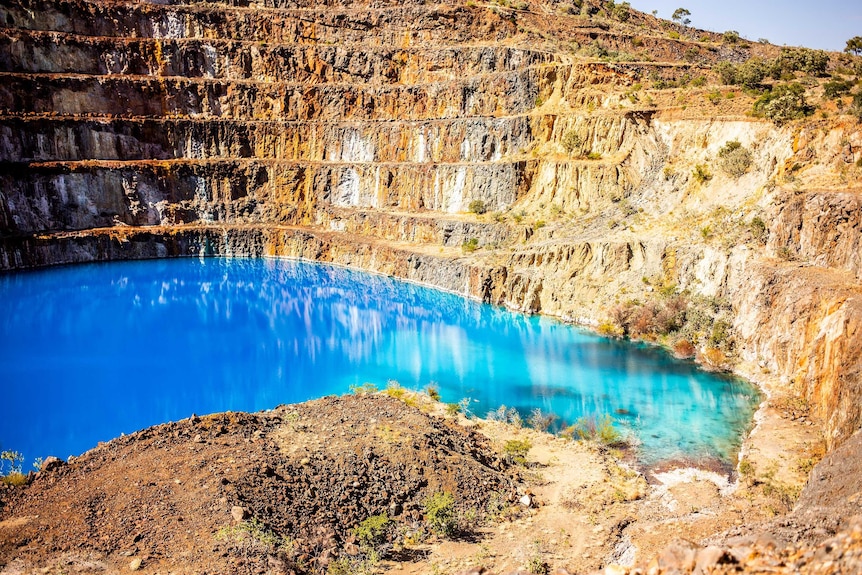 A picture of an old mine pit, showing each level of the mine, with bright blue and green water at the base.