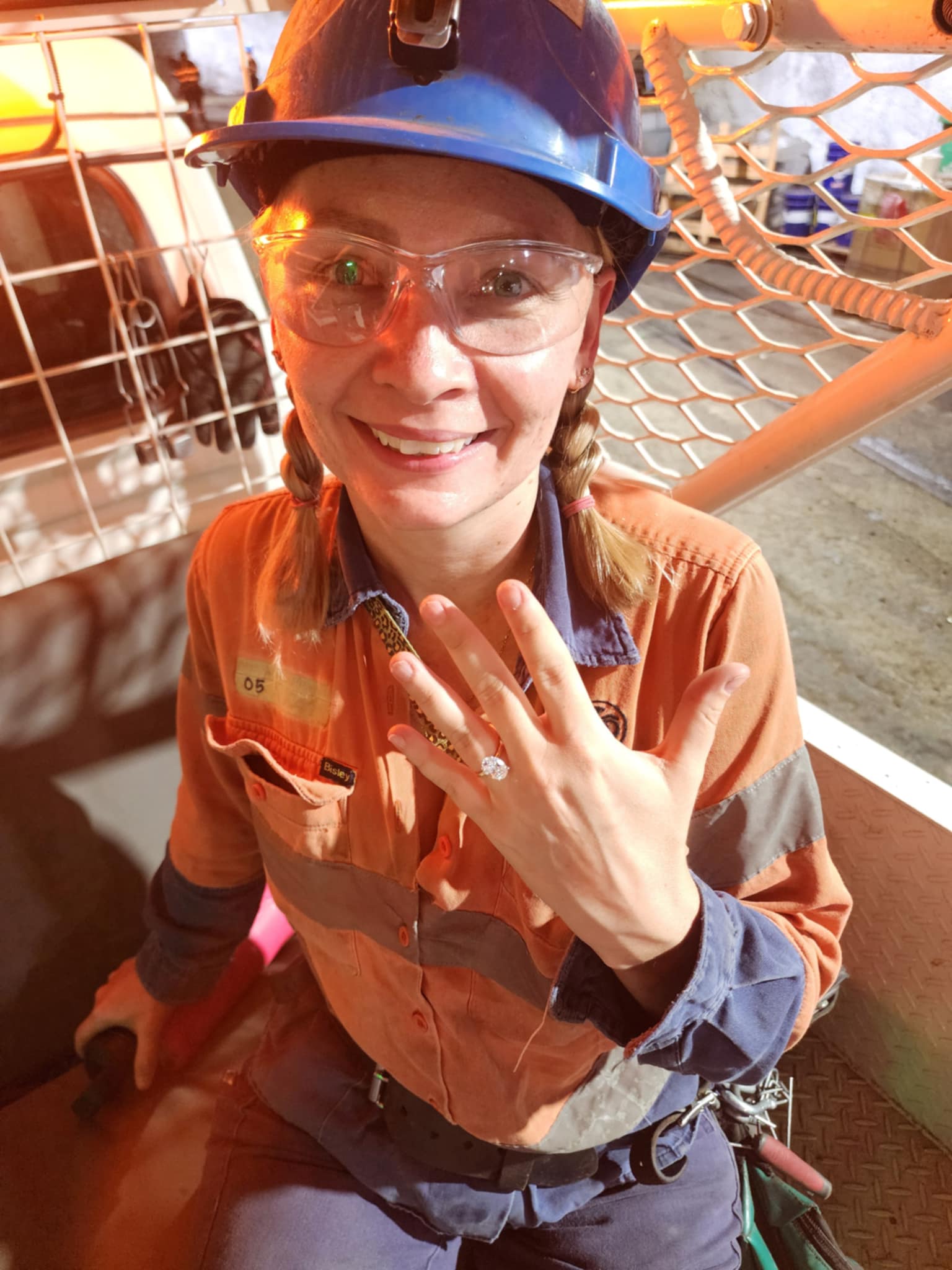 A young woman smiles with her hand raised showing a diamond ring