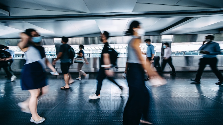 A blurred image of commuters in face masks walking during rush hour.