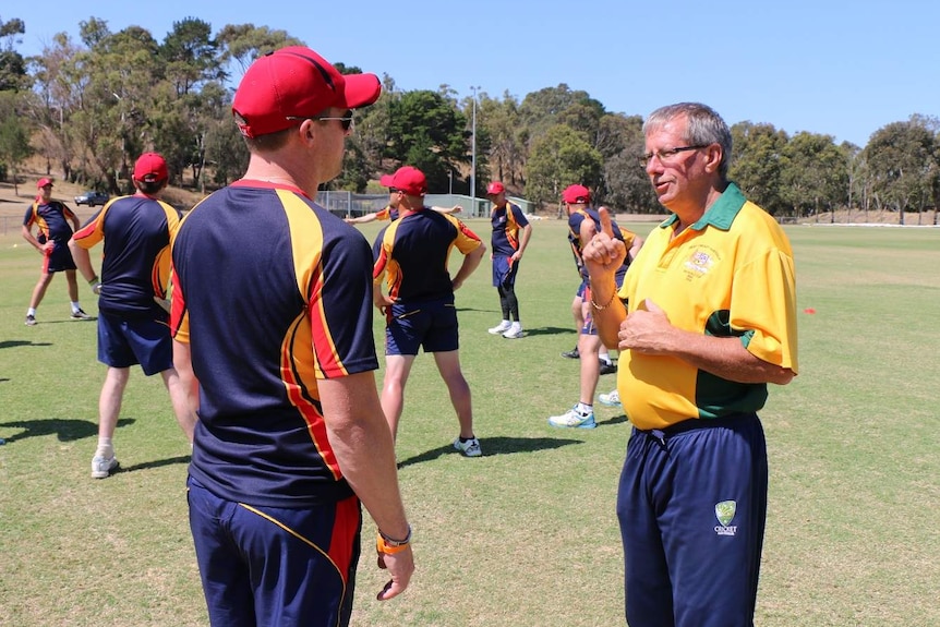 A man in a yellow shirt with cricket players stretching on lawn